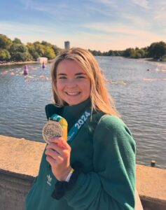 Anna holding a medal, smiling in front of the Serpentine Lake.